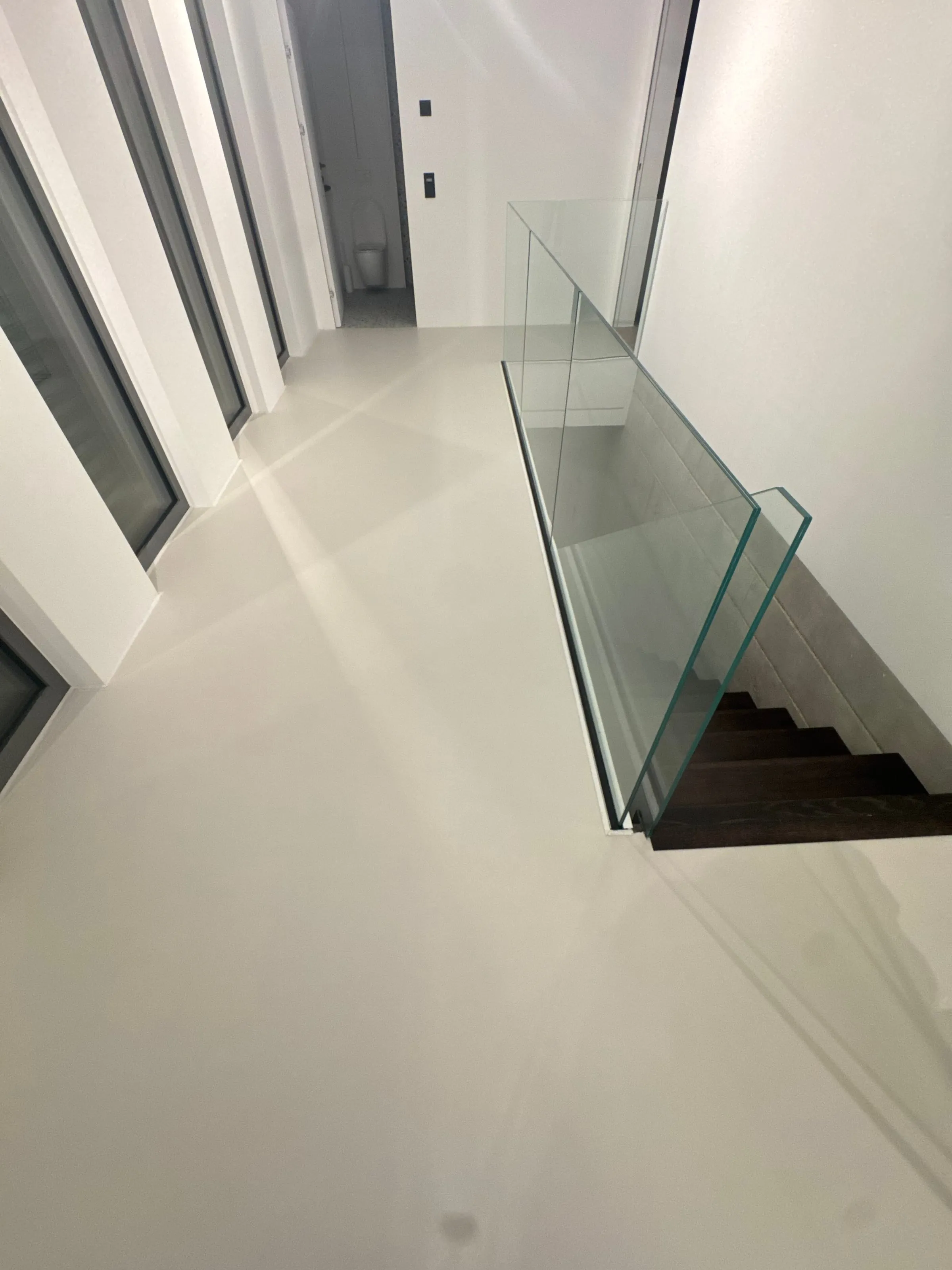 Schody ze szklaną balustradą i posadzka z mikrocementu